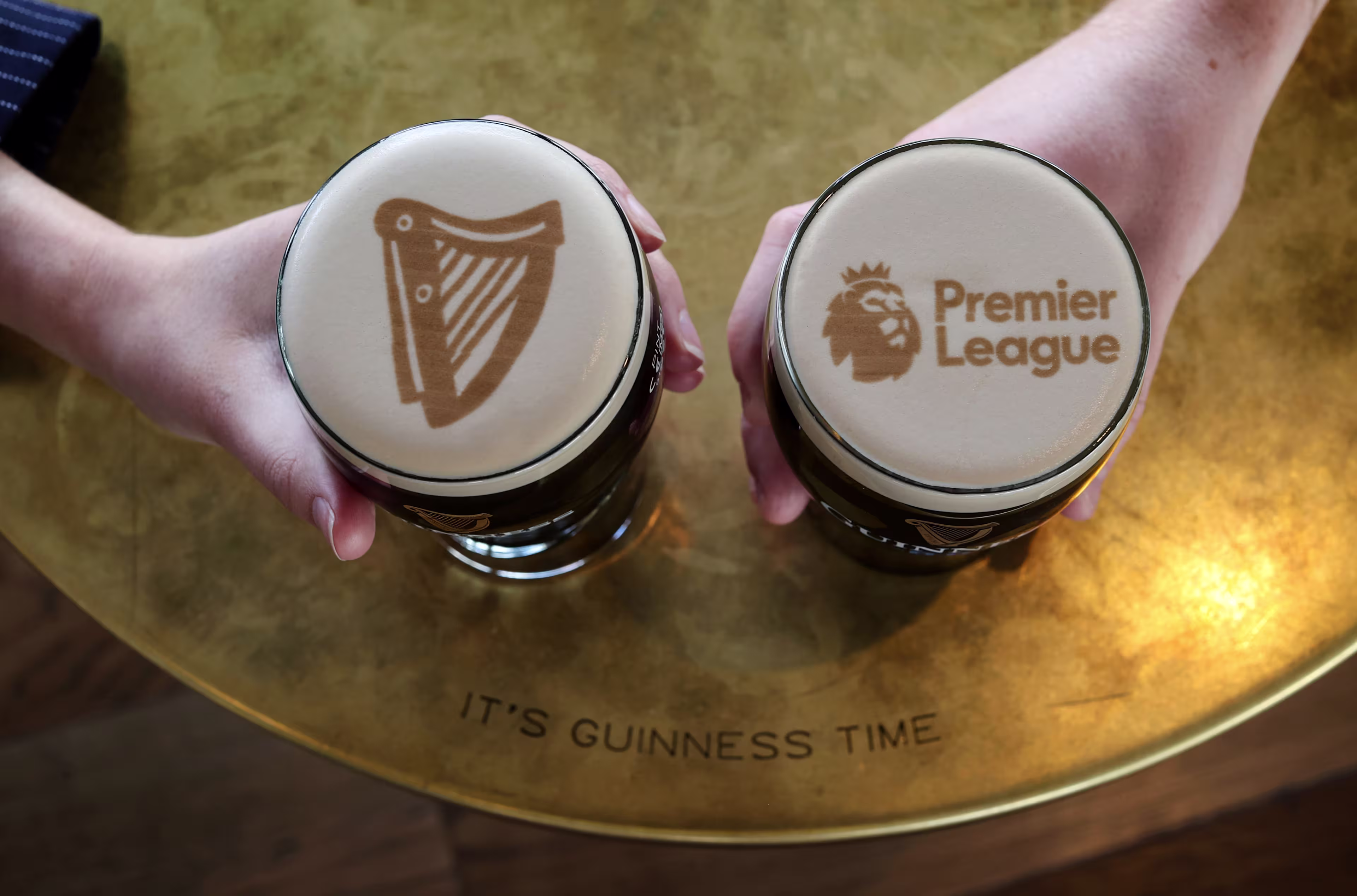two people holding two beer glasses with the words guinness and premier league