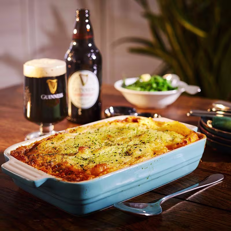 there is a blue dish with a casserole and a glass of beer