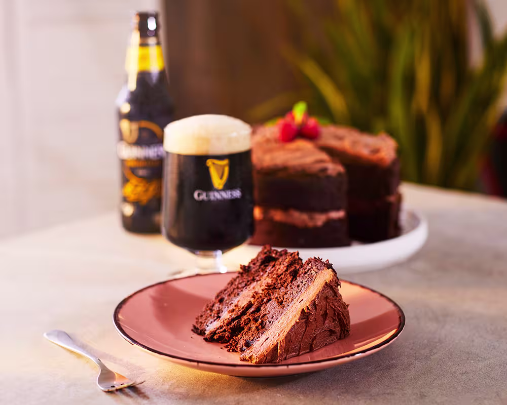 there is a piece of cake on a plate with a beer in the background