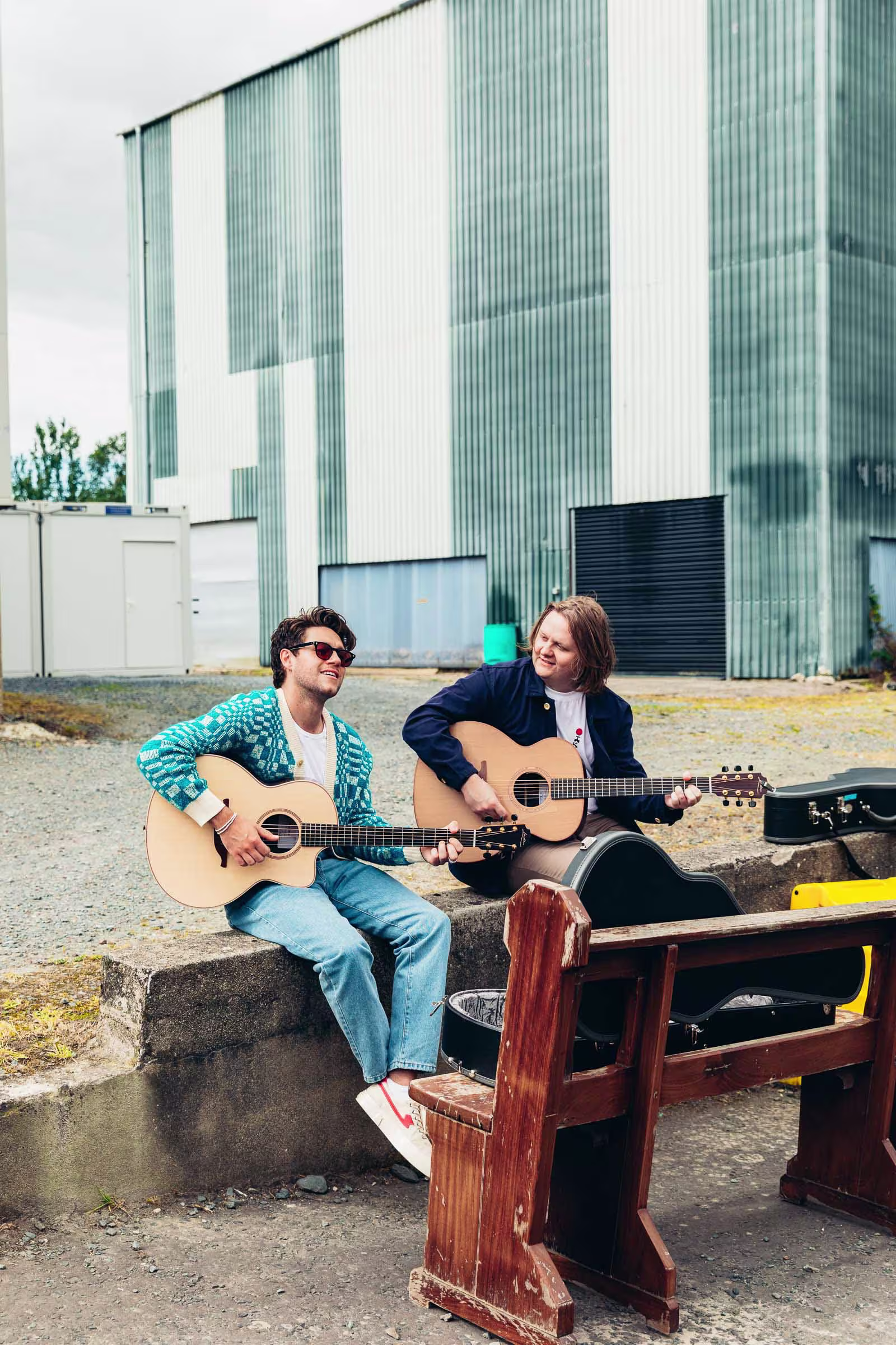 there are two people sitting on a bench playing guitars