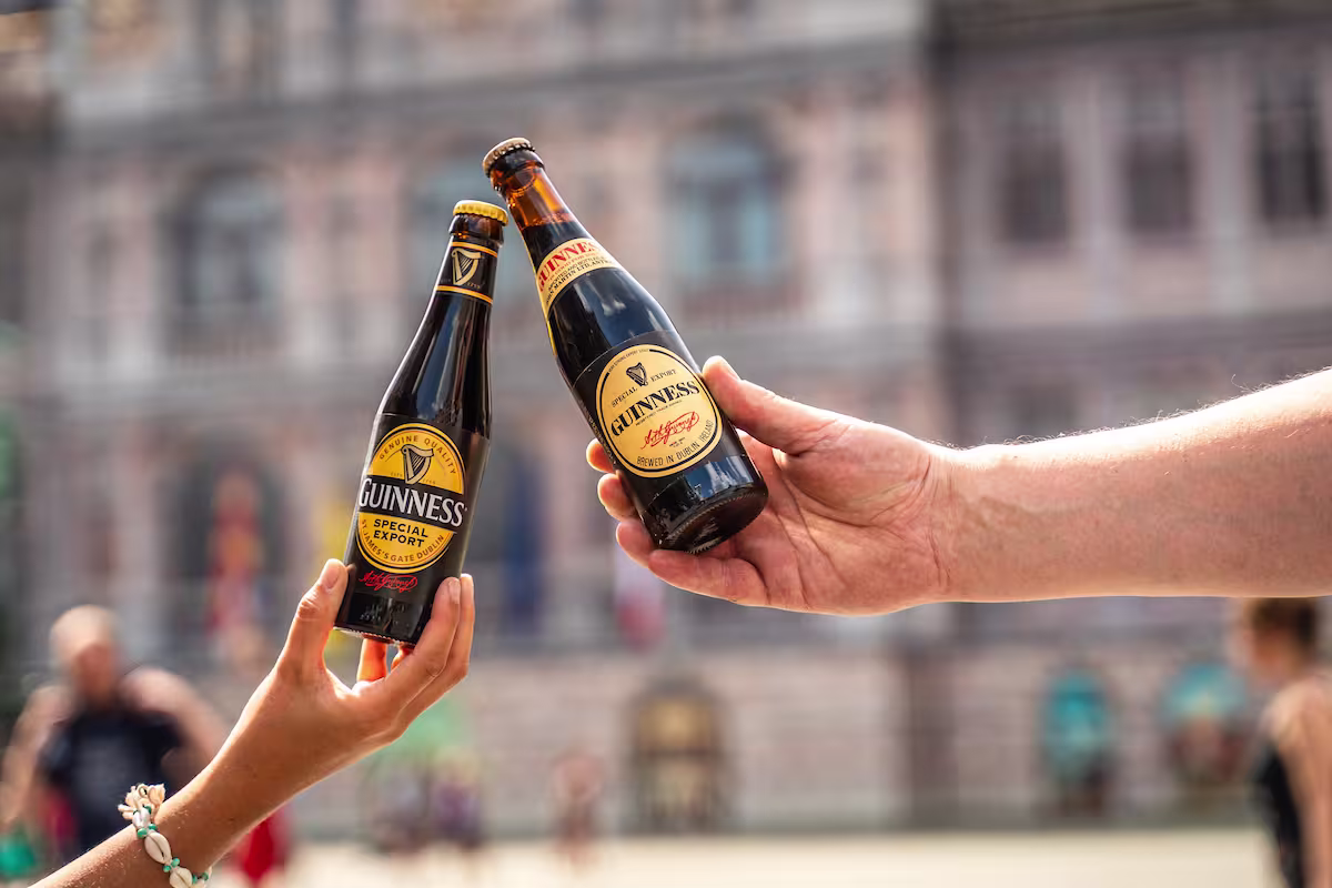 someone holding two bottles of beer in their hands in front of a building