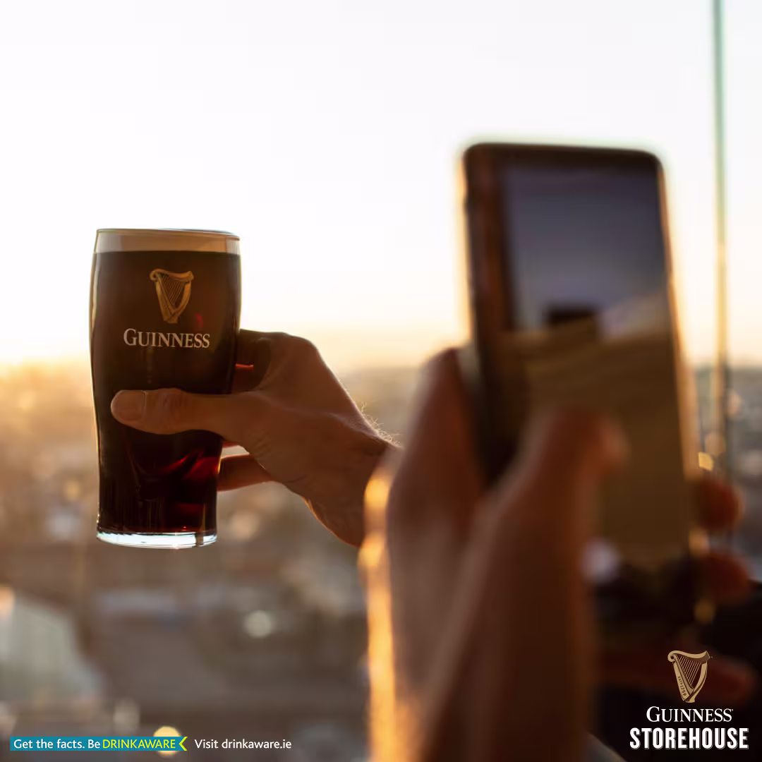someone holding a glass of Guinness beer in their hand while looking at a cell phone