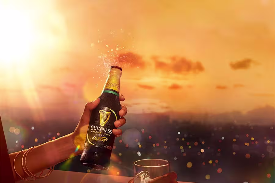 someone is holding a beer bottle and a glass with a sunset in the background