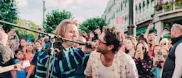 there are two men singing and playing guitar in front of a crowd