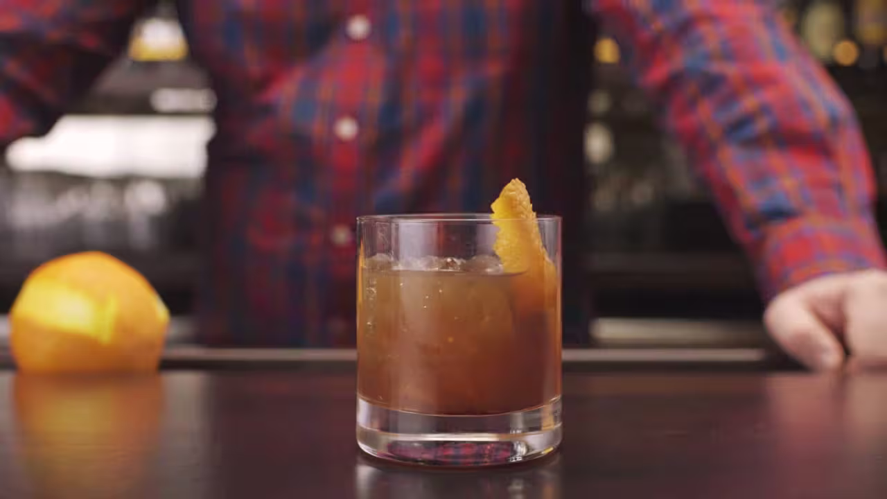 someone is making a drink with a orange peel in a glass