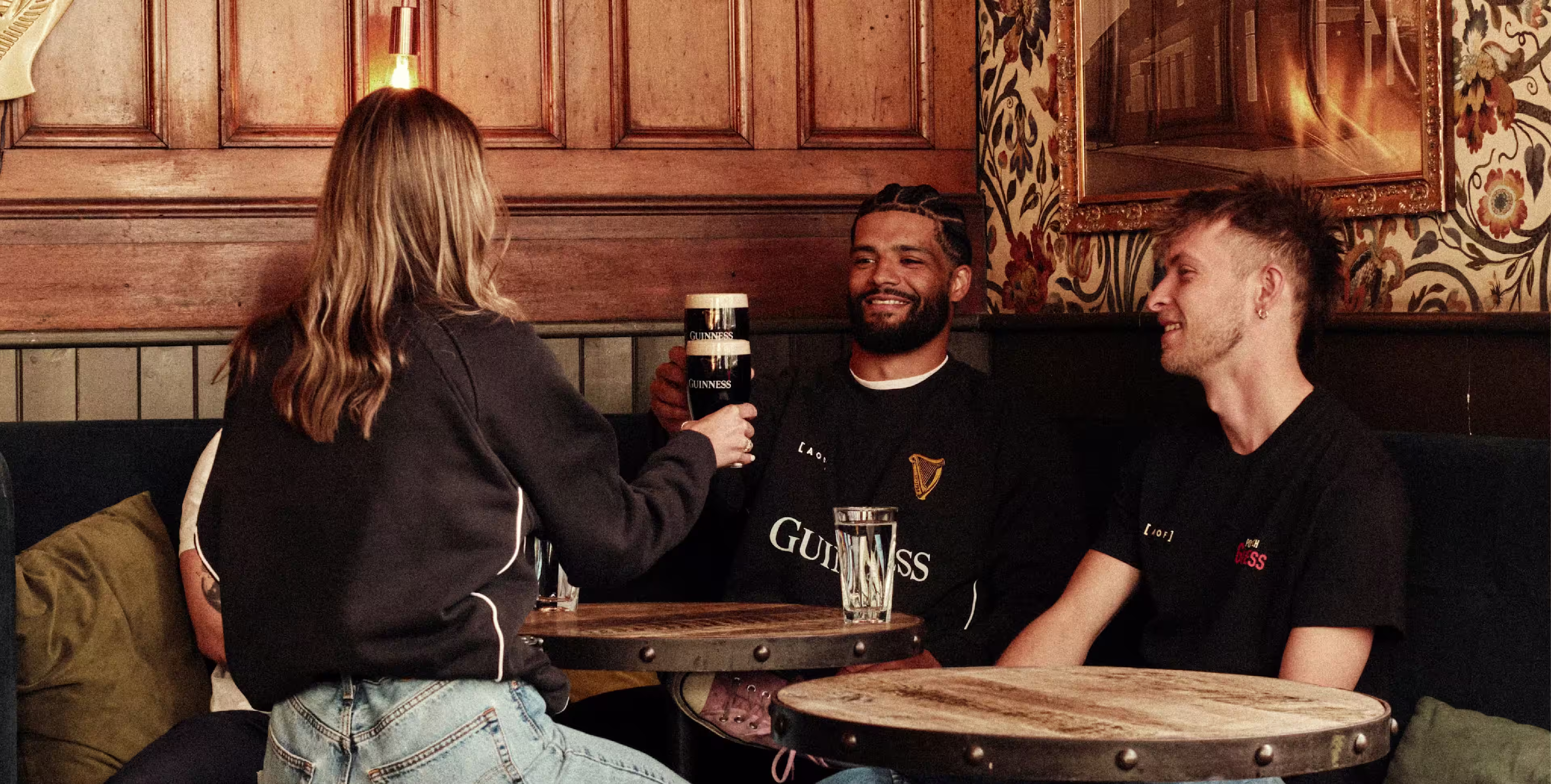 People at the bar cheering with a Guinness poured into Guinness glass and wearing Guinness merch
