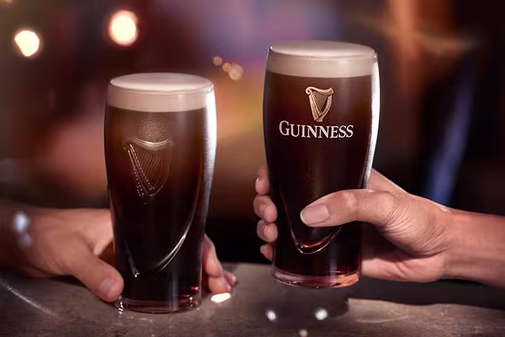 there are two people holding glasses of beer at a bar