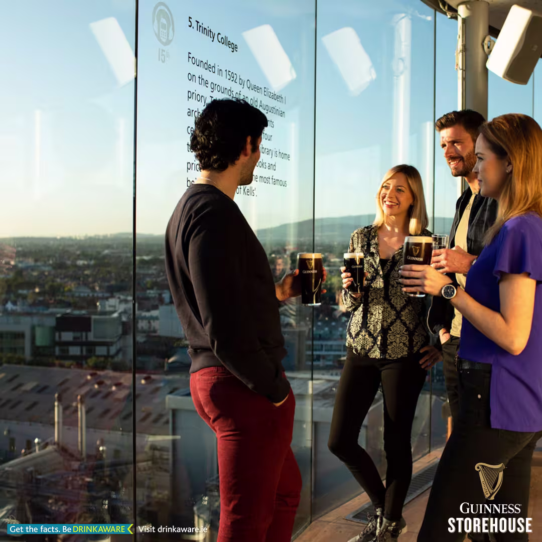 three people standing in front of a glass wall drinking beer