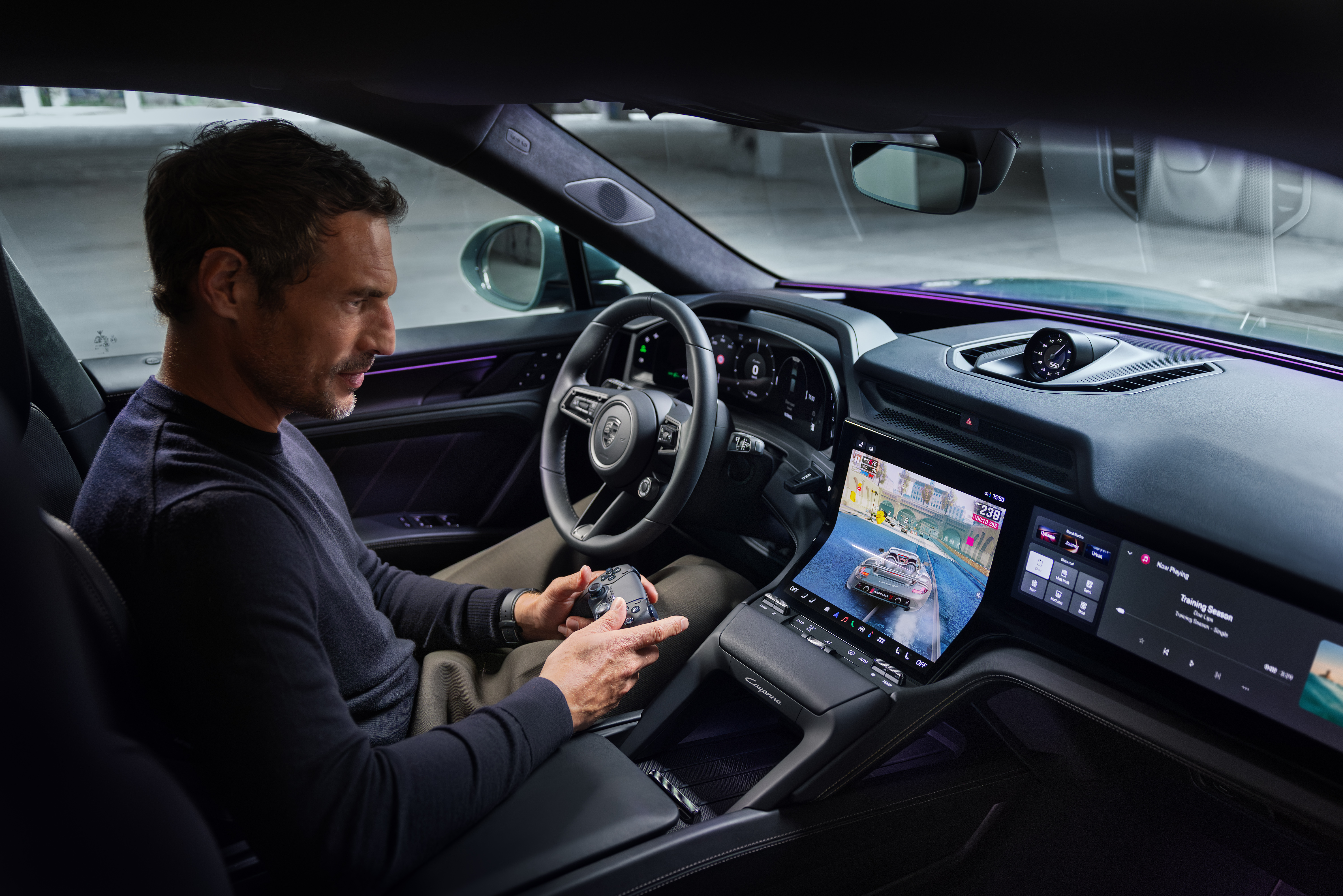 A man and woman are driving along a scenic coastal road in a Porsche. The woman is behind the wheel, wearing sunglasses, while the man in the passenger seat interacts with the central touchscreen. The dashboard displays navigation and media content, including a video of a car driving at sunset. The digital instrument cluster shows a speed of 50 km/h. The ocean and rugged cliffs are visible through the windshield, reflecting a peaceful, high-tech driving experience.