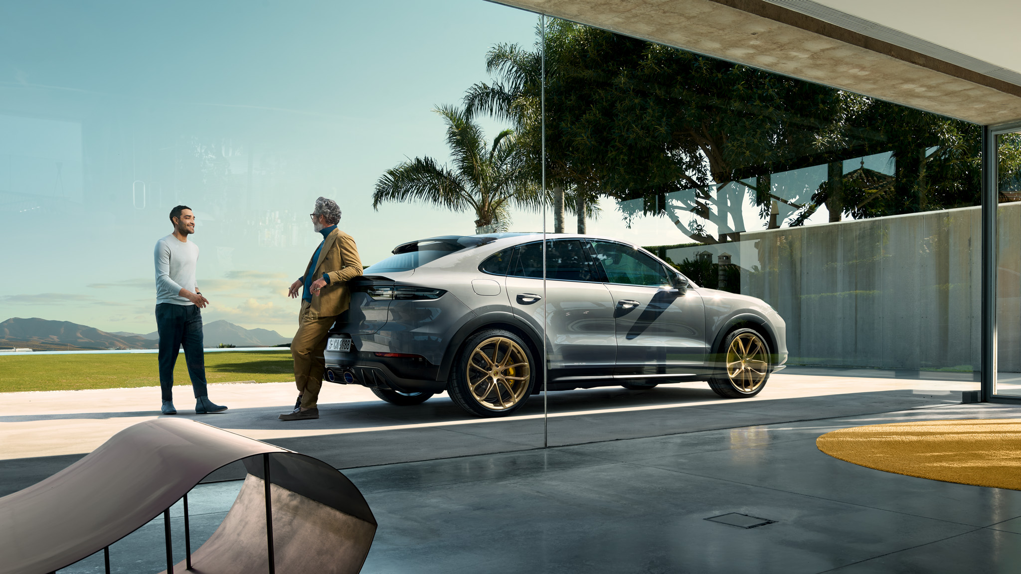 Two men talking in front of a grey Porsche Cayenne