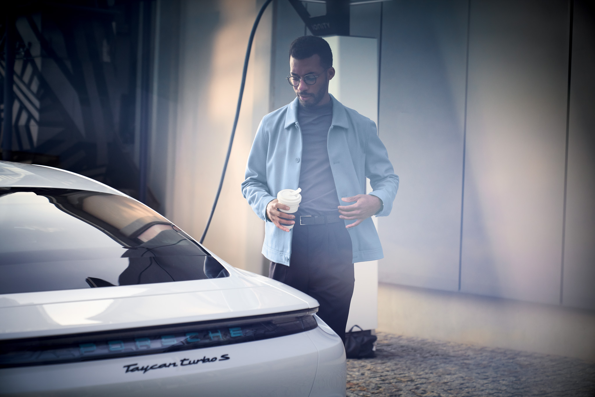 Man holding a coffee mug walking towards white Porsche Taycan