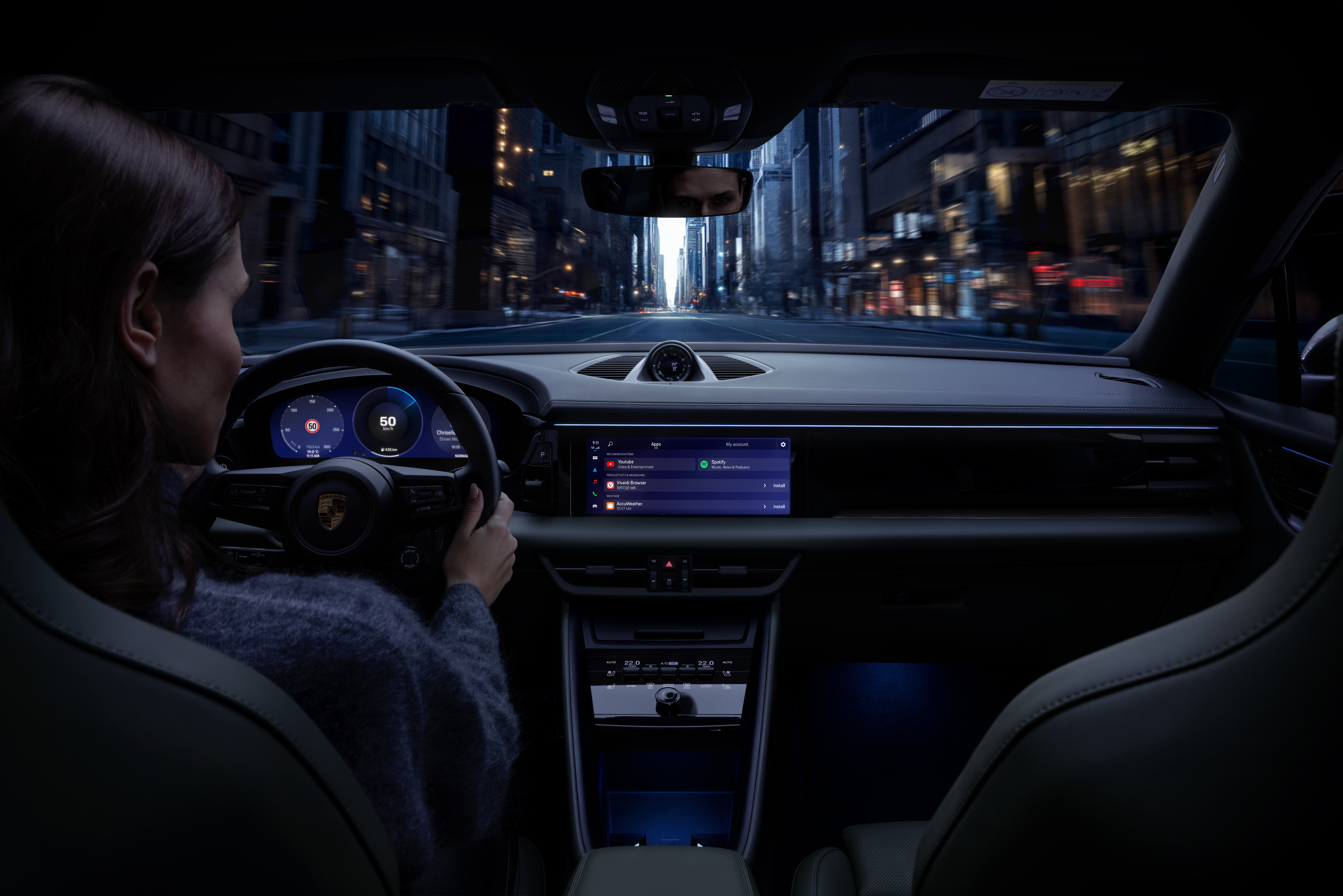 Inside a Porsche, a woman drives. A city street is visible ahead. The dashboard is modern with digital displays.