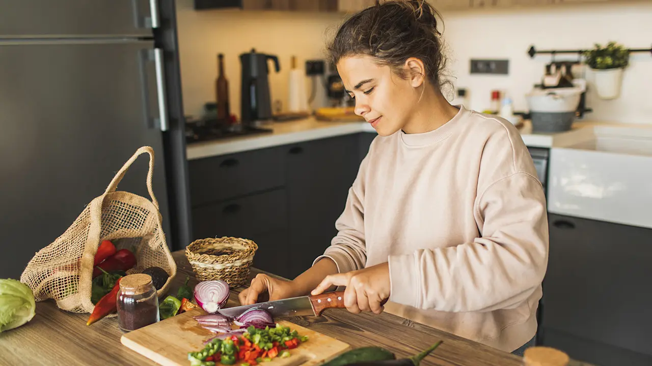 A person chops fresh food and vegetables on a cutting board while preparing a meal in a modern home kitchen.