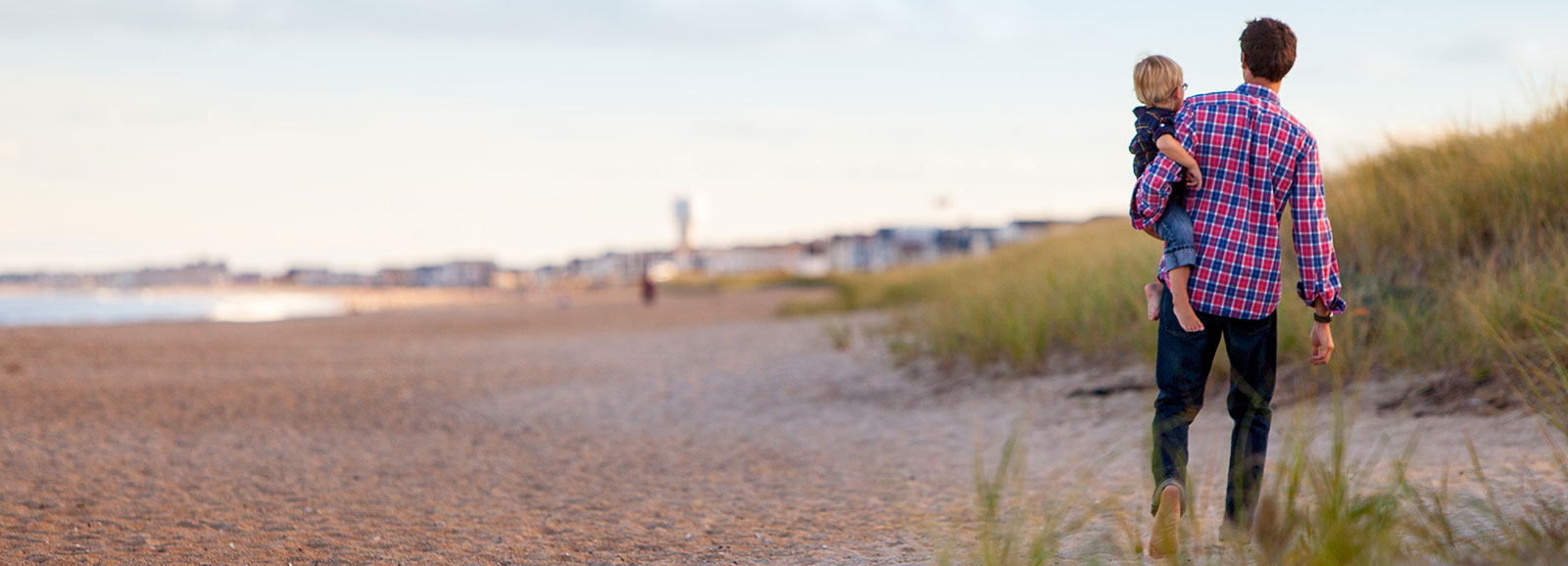 father holding a child while walking on sand