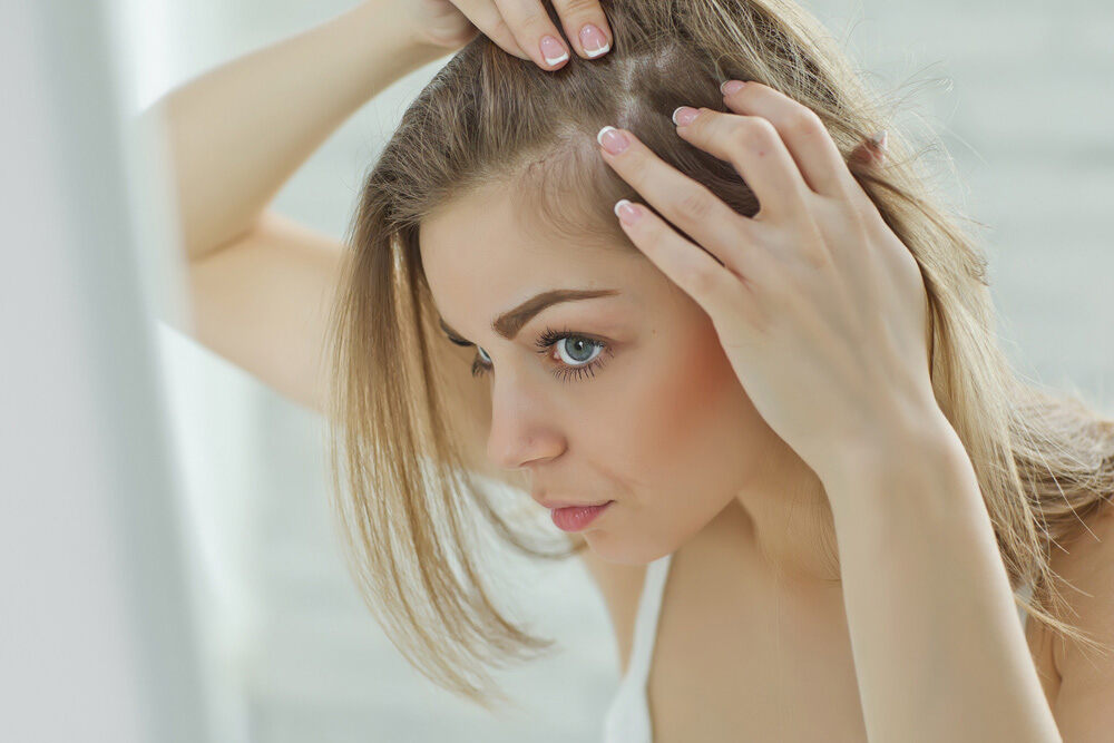 jeune femme blonde inspectant son cuir chevelu pour perte de cheveux