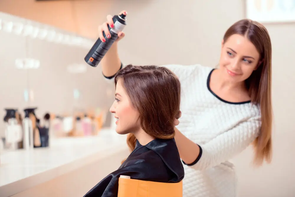 a female hair stylist spraying her client’s hair with hair spray