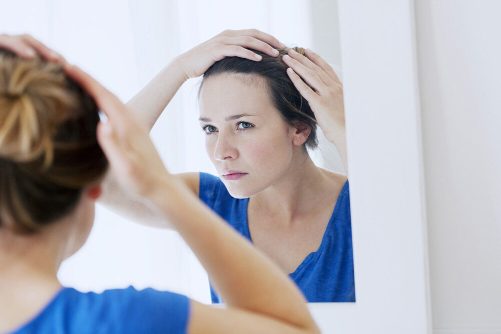 woman looking in the mirror trying to find out the root cause of hair loss