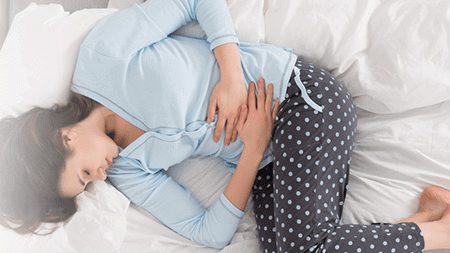 Woman on a bed with hands on her stomach