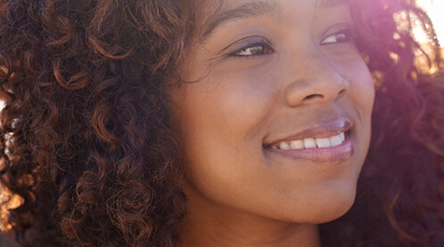 Jeune femme noire aux cheveux bouclés qui regarde au loin et sourit