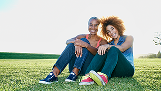 Two women sitting in a park together and smiling