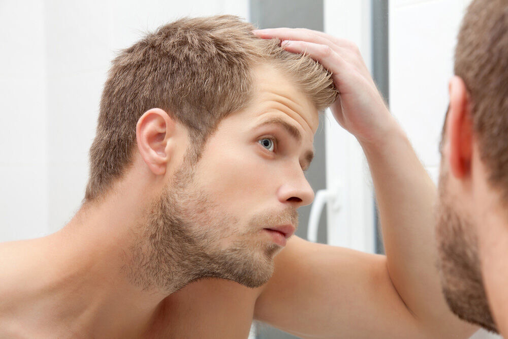 young man looking at his hair line in the mirror