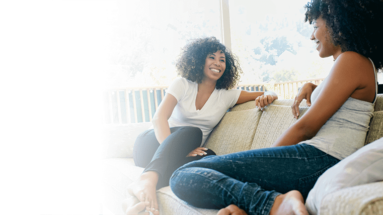 Two women sitting on a sofa together and smiling