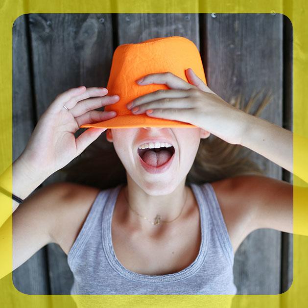 girl covering half of her face with an orange hat