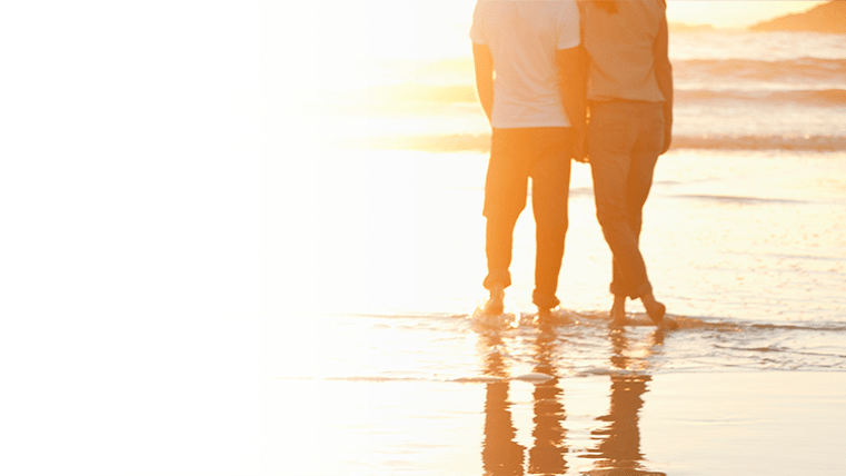 Silhouette of a couple watching the sunset while holding hands on the beach