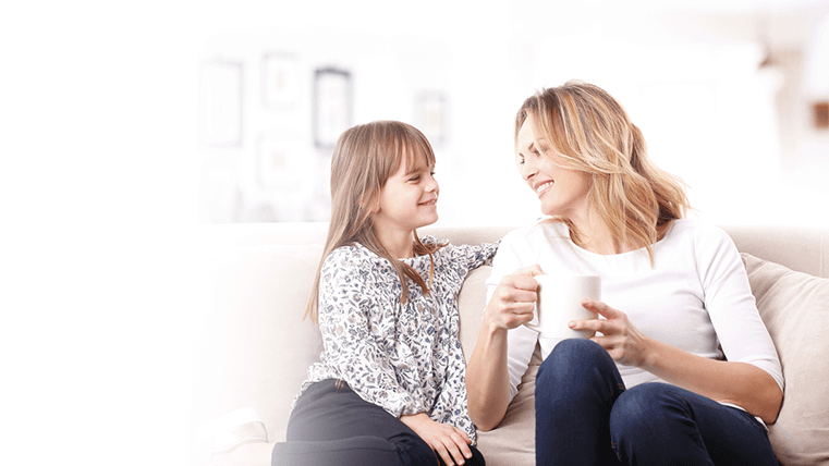 Mother and her young daughter sitting on a couch smiling