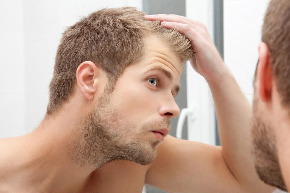 jeune homme qui regarde ses tempes dans un miroir