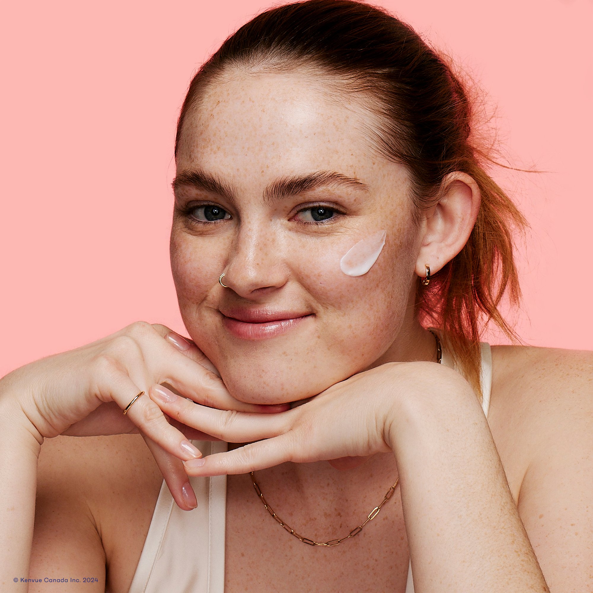 Young woman with face moisturizer smear on her left cheek smiling