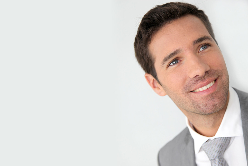 man with dark hair smiling in a grey suit