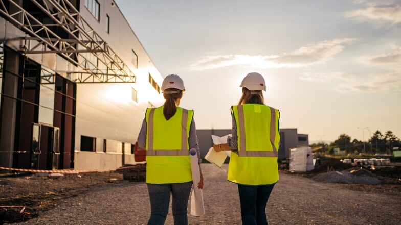 Women contractors walking towards a building with blueprints on their hands