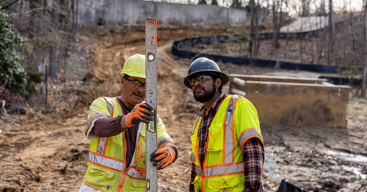 Two construction workers wearing safety vests and helmets holding a level on site