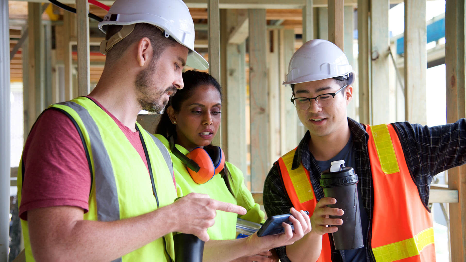  photo of 3 construction workers discussing plans and using the Procore app on their mobile device
