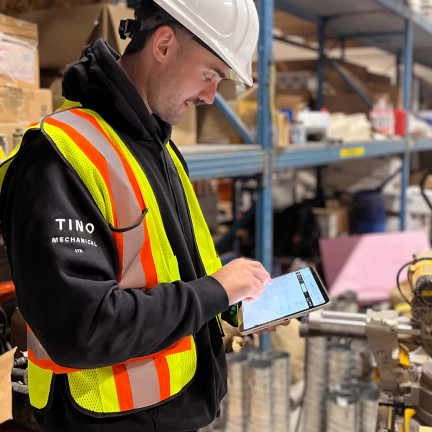 a person in a hard hat and vest looking at a tablet