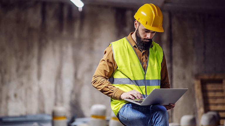 Man using procore on a laptop at a construction site