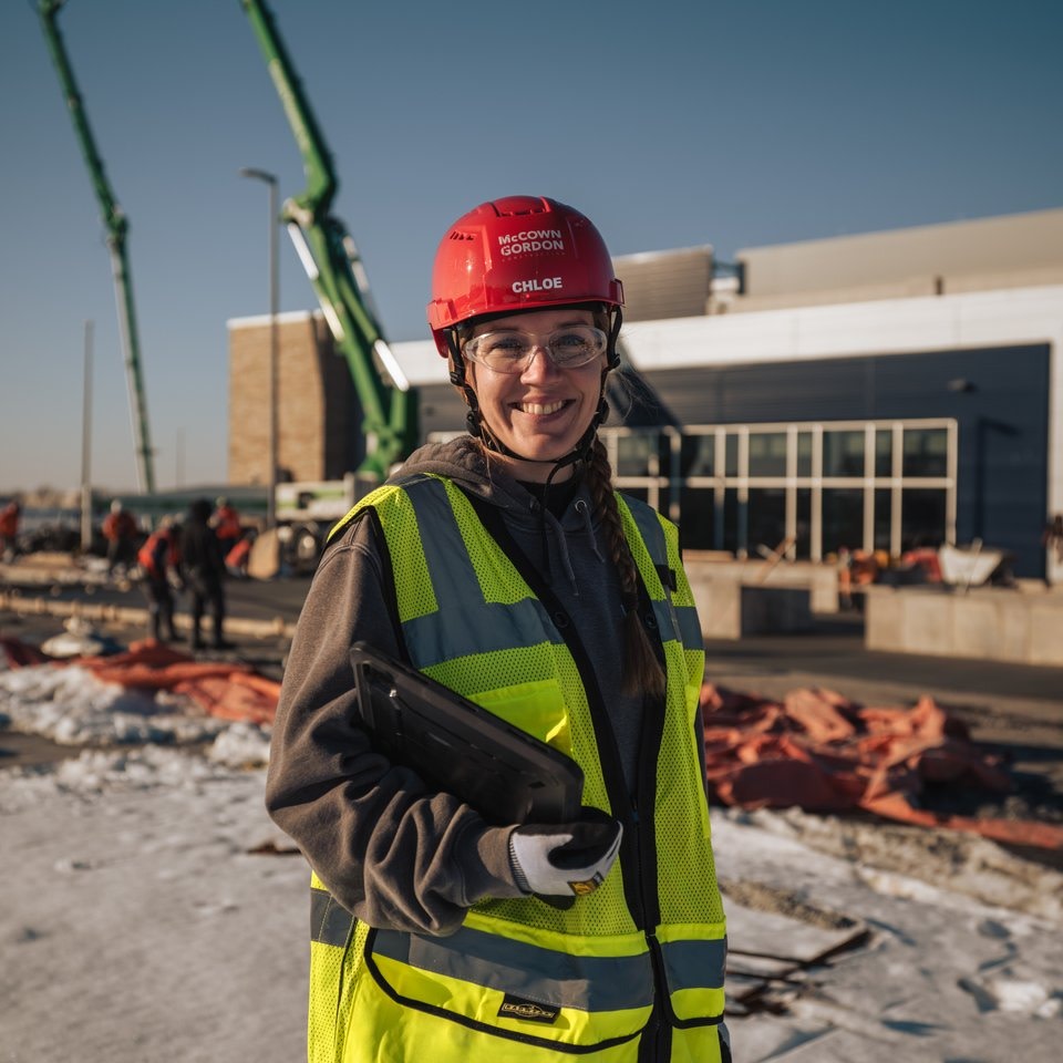 Smiling female construction worker in red helmet and yellow vest on site