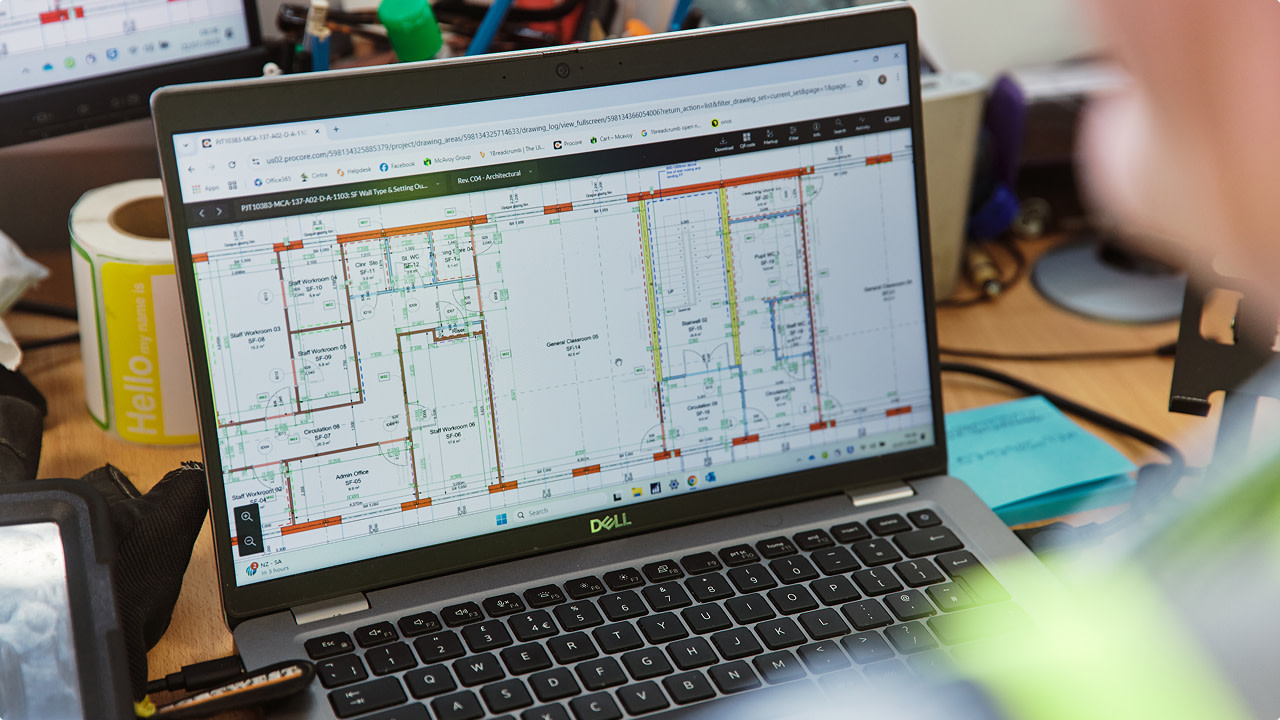 Laptop screen displaying architectural floor plans on a cluttered desk.