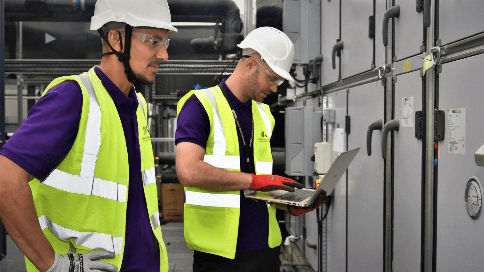 A couple of men wearing safety vests and helmets looking at a laptop