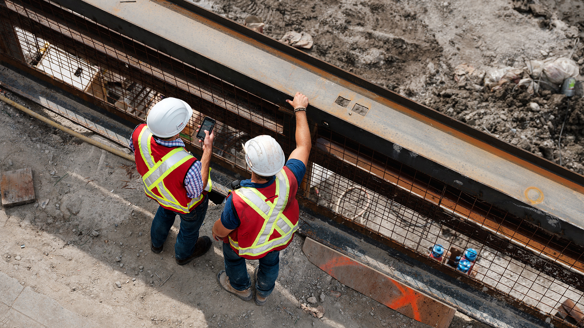 Aerial view of two men wearing safety vests and helmets standing on a bridge