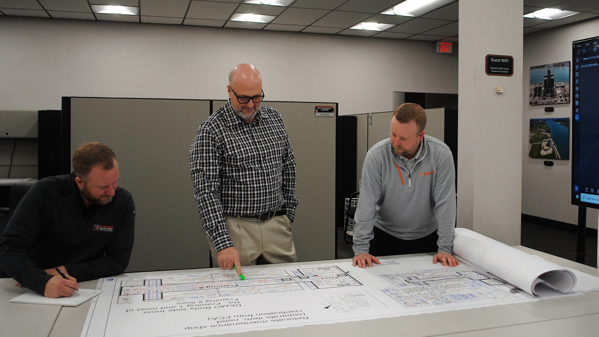 a group of men standing around a table looking at a blueprint