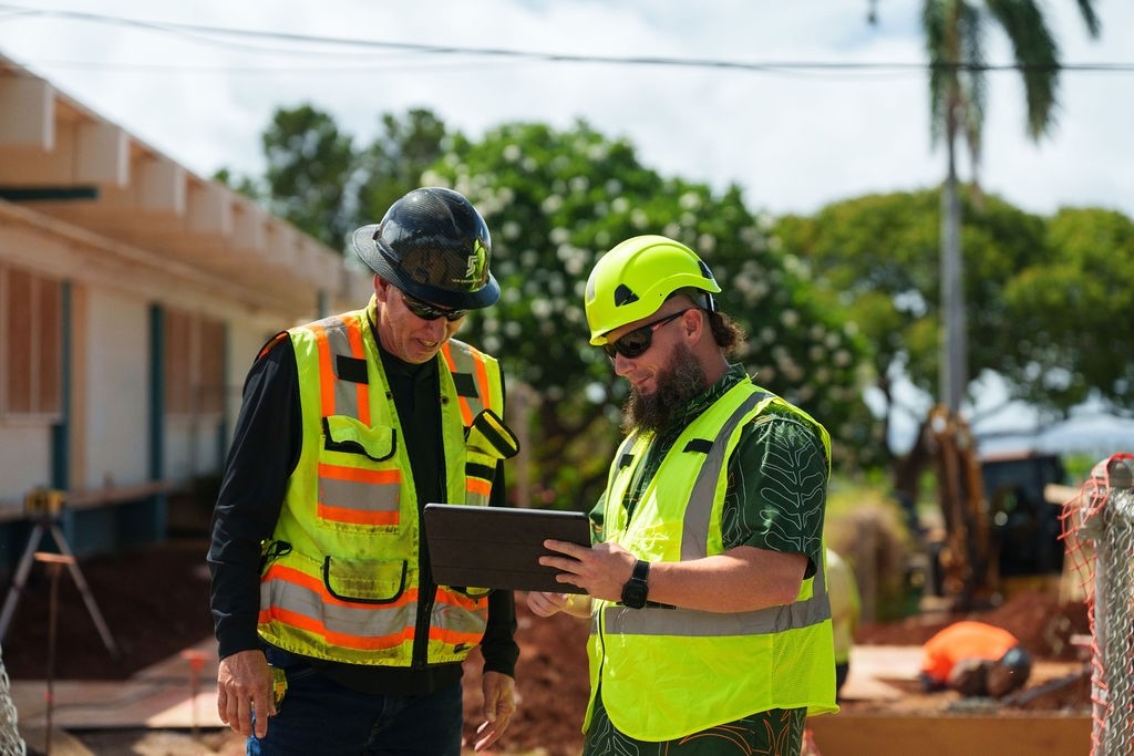 The project manager and superintendent on a construction site in Hawaii review project data on a smart tablet.