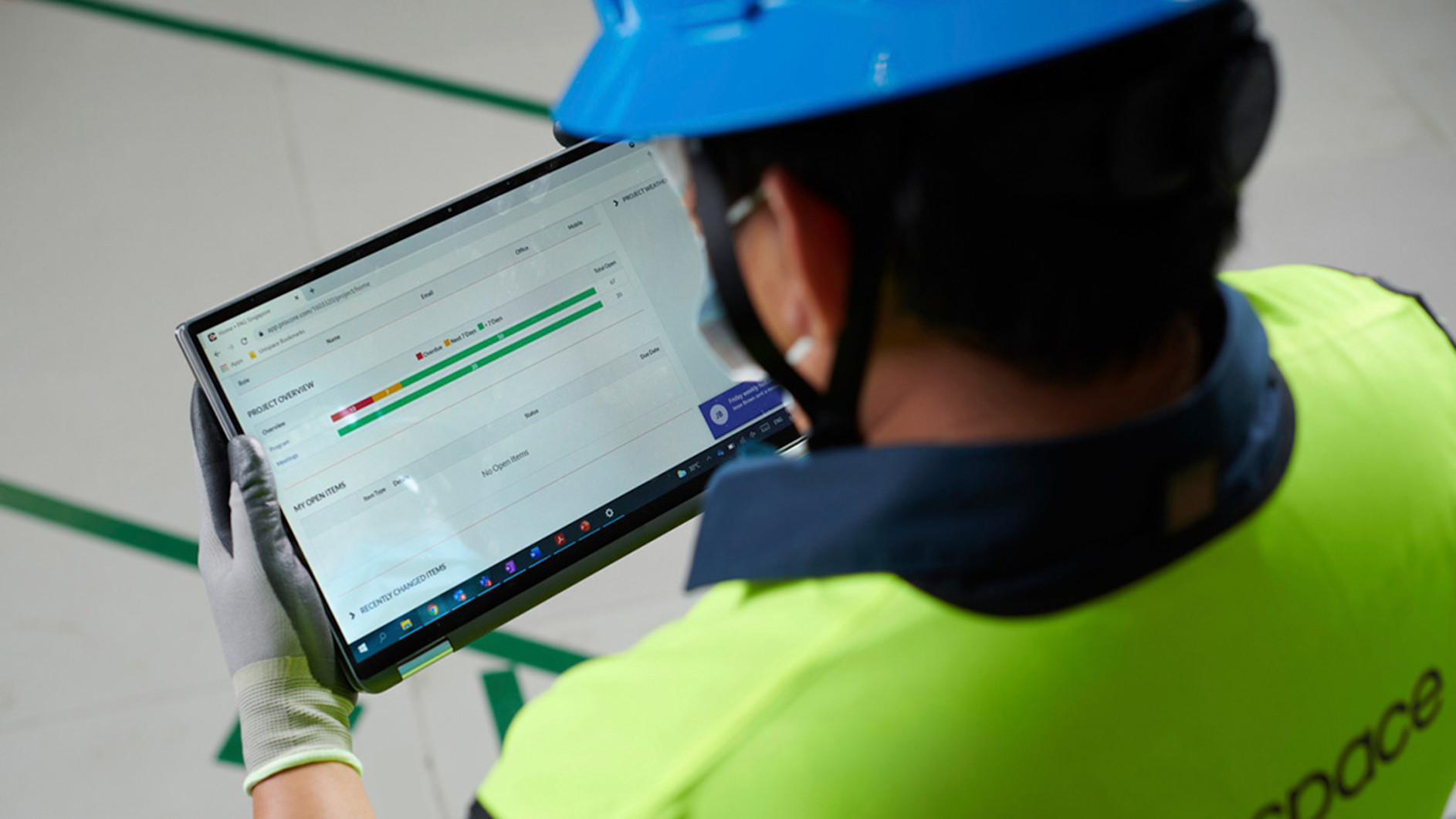 Construction worker in safety gear reviewing project data on tablet device