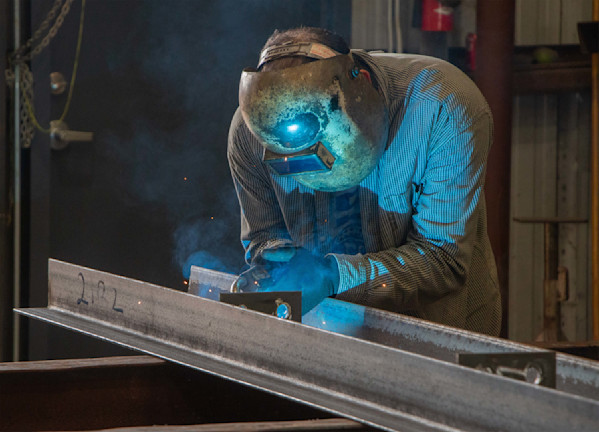 Welder in protective gear welding a metal beam with blue sparks and smoke