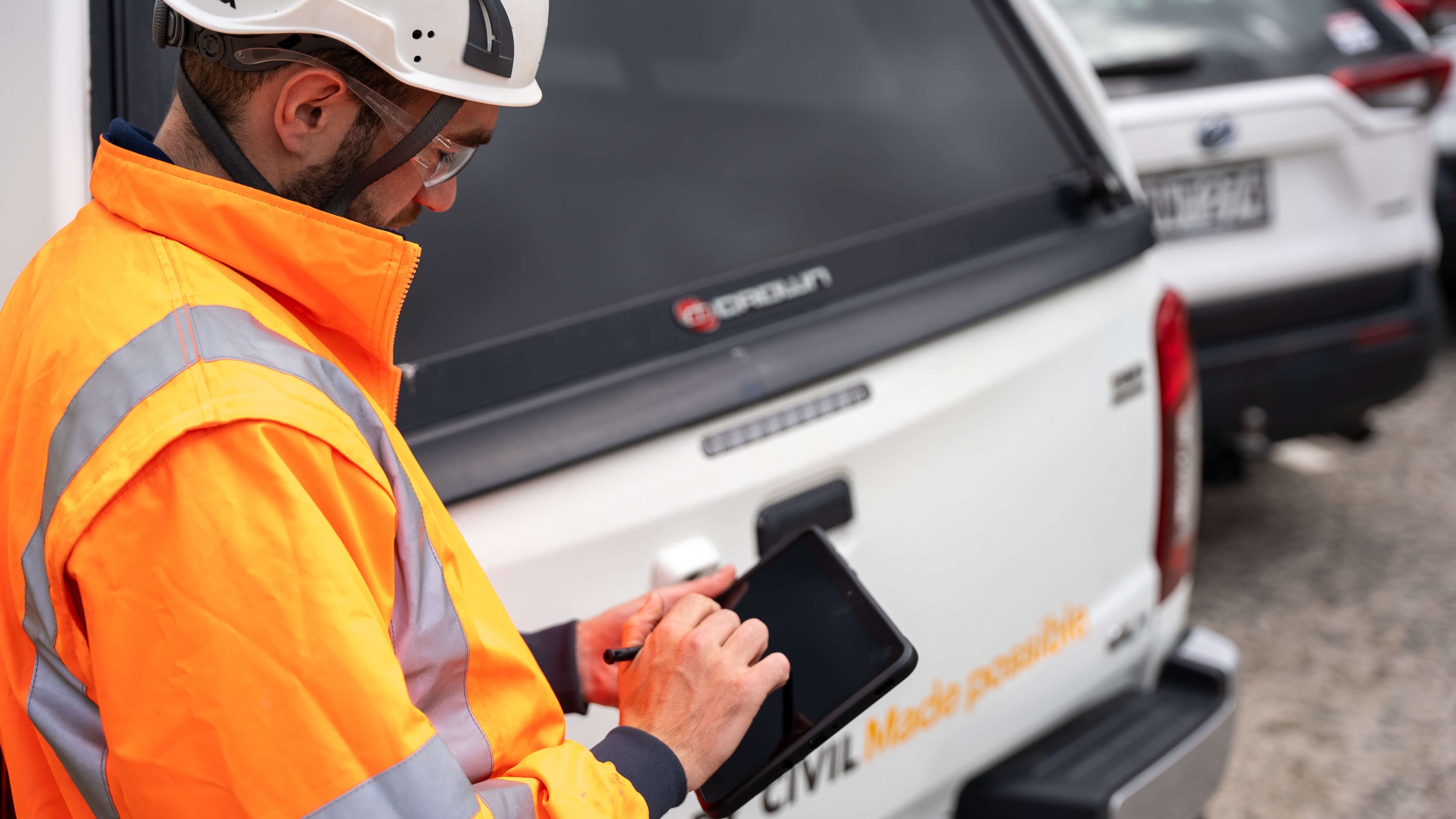 A construction worker using a tablet while standing next to a car