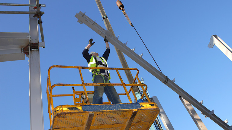 construction worker erecting large metal framework atop a lift