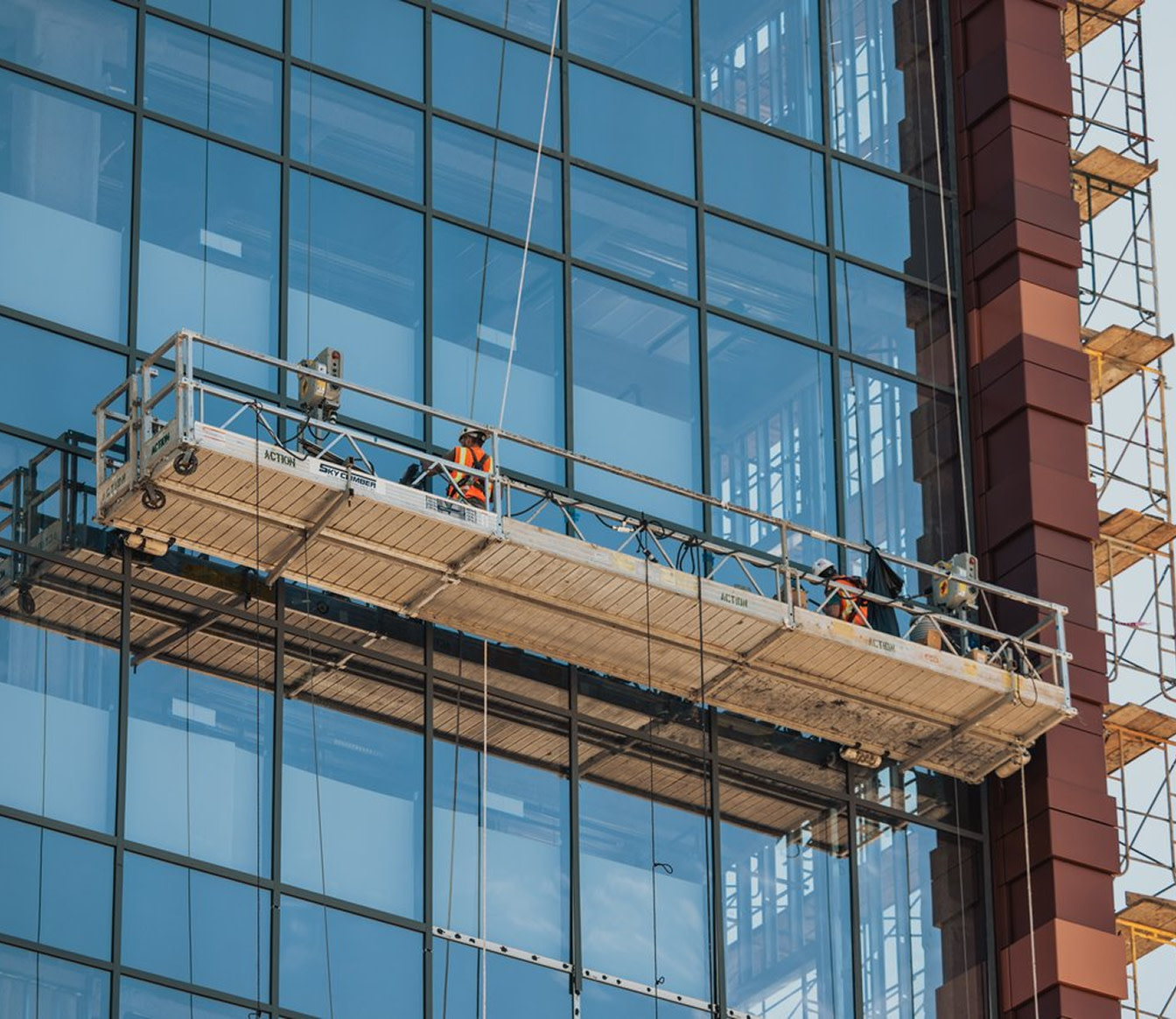 Workers suspended on a platform cleaning a glass building facade