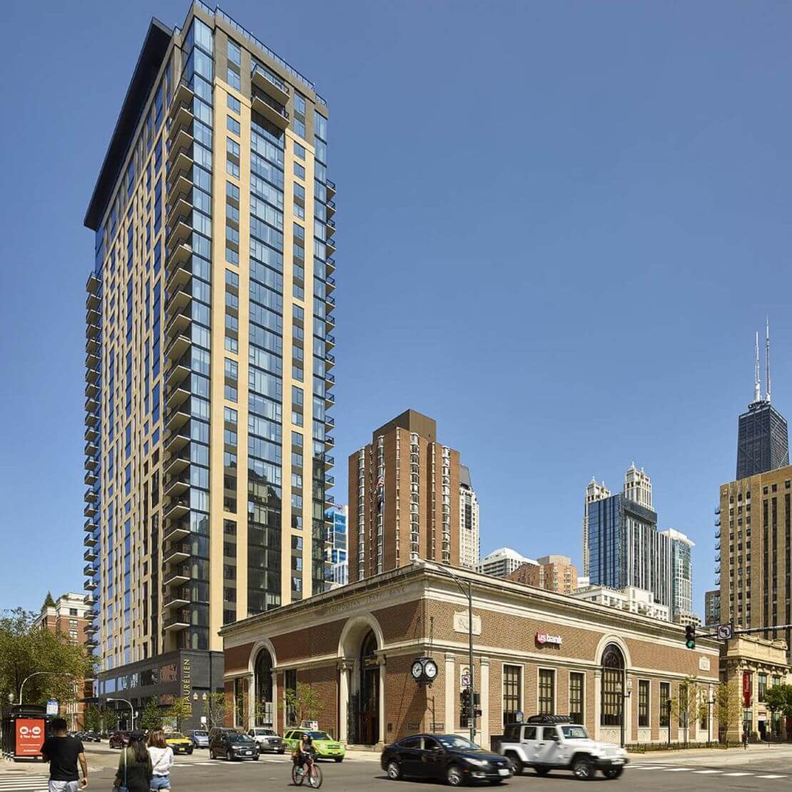 Corner of a street with cars and people moving, street level shops and a glass building behind