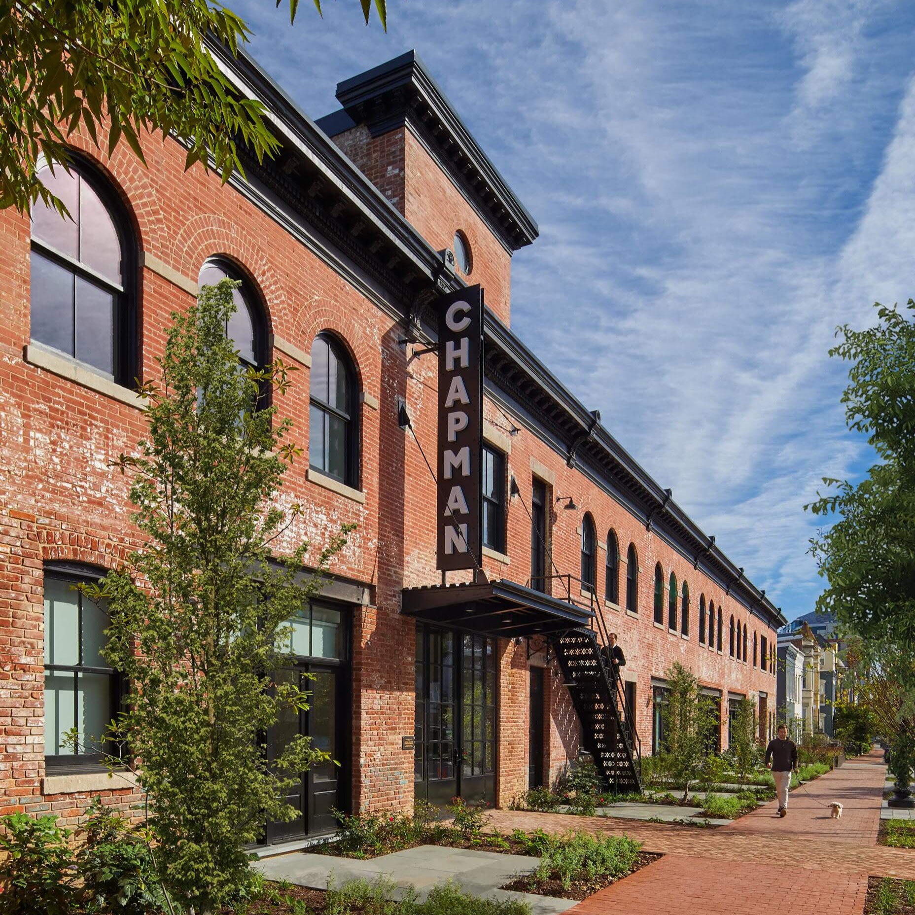 a brick building surrounded by trees and a man walking by.